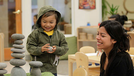 A teacher observes a young boy stacking toy rocks.