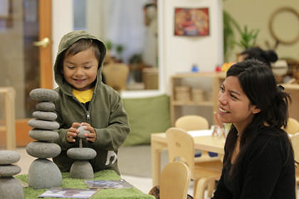 A teacher observes a young boy stacking toy rocks.